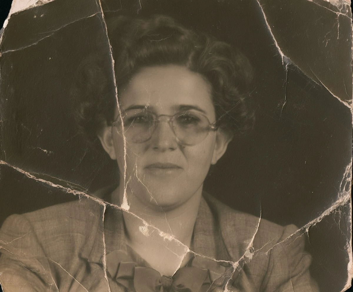 Black-and-white photo of a woman in glasses before AI restoration